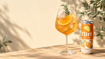 Verre de spritz à l'orange sur glace avec romarin, à côté d'une canette de limonade pétillante Flirt Clémentine, sur une table de terrasse
